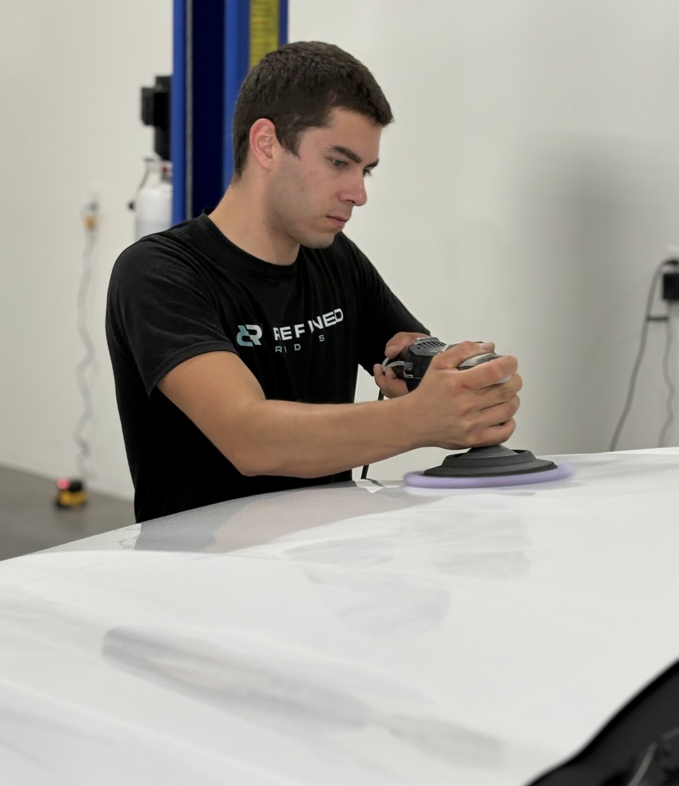 Refined Rides technician machine-polishing a white vehicle panel during paint correction in Yakima, WA