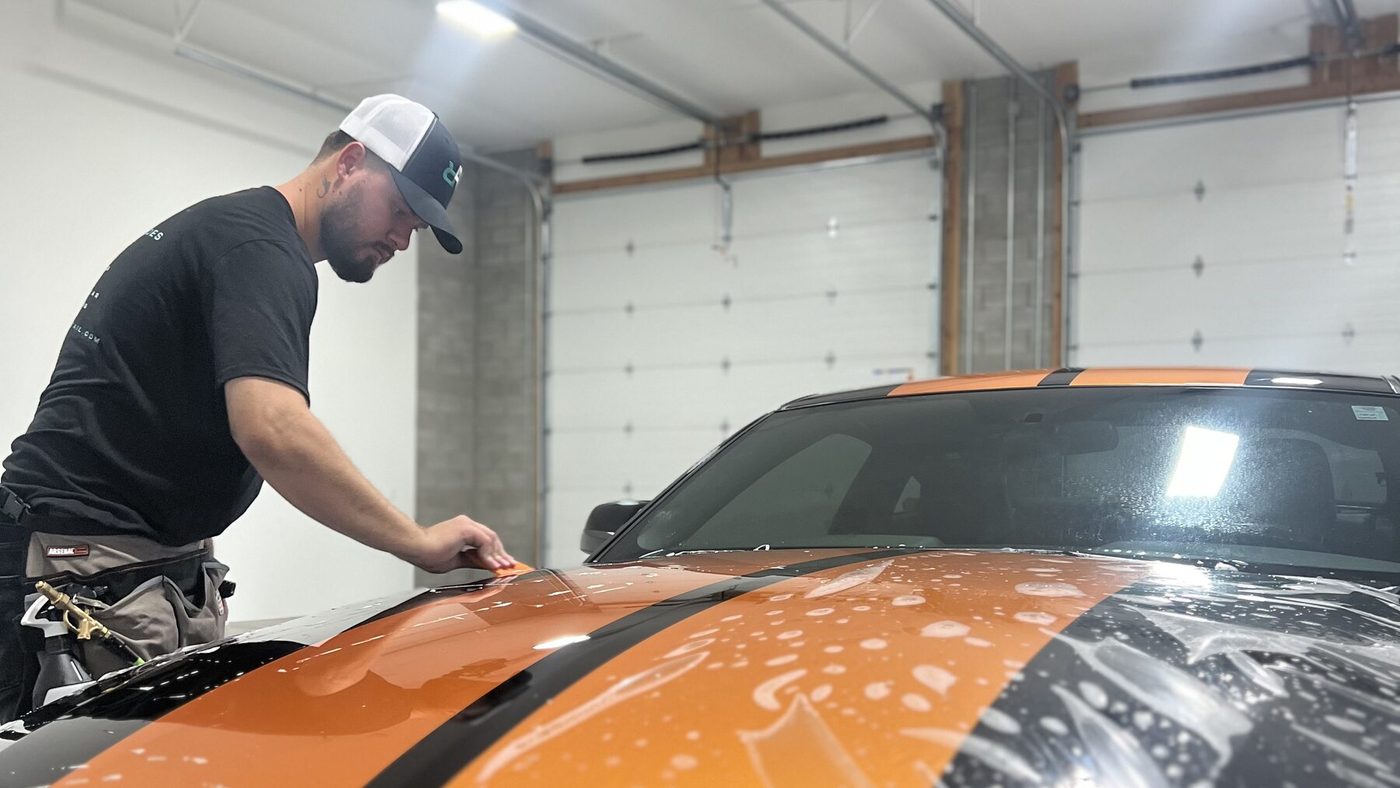 Refined Rides technician applying paint protection film to a black Mustang with orange racing stripes in Yakima, WA